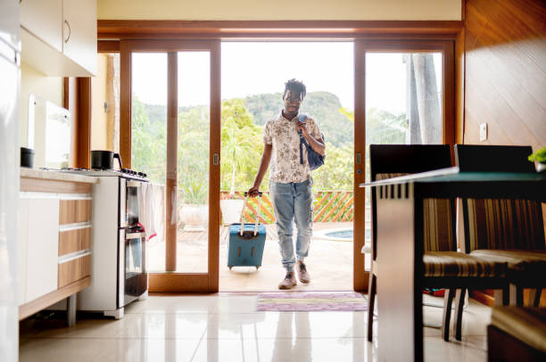 homme avec une valise traversant les portes-fenêtres de son logement - maison de vacances photos et images de collection