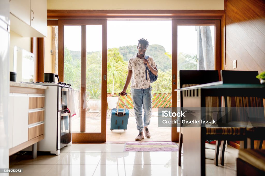 Man with a suitcase walking through the patio doors of his accommodation Young man walking through the patio doors of his rental accommodation pulling a wheeled suitcase Vacation Rental Stock Photo