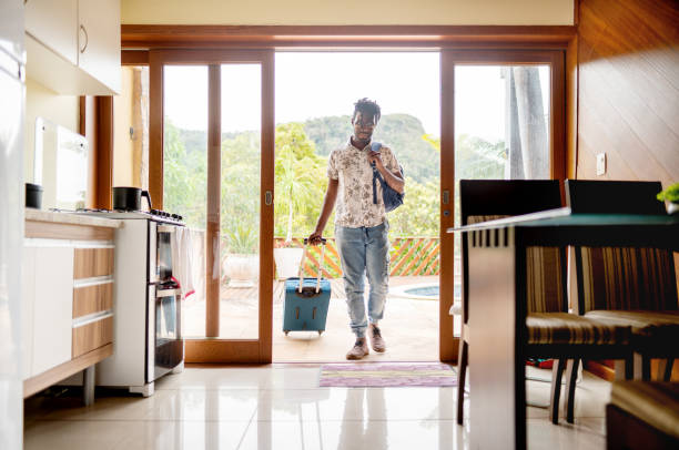 Man with a suitcase walking through the patio doors of his accommodation Young man walking through the patio doors of his rental accommodation pulling a wheeled suitcase airbnb stock pictures, royalty-free photos & images