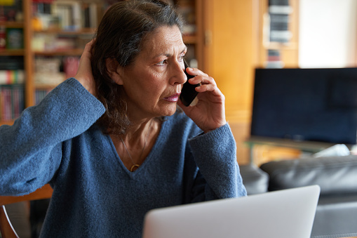 Stressed senior businesswoman on the phone while working on laptop