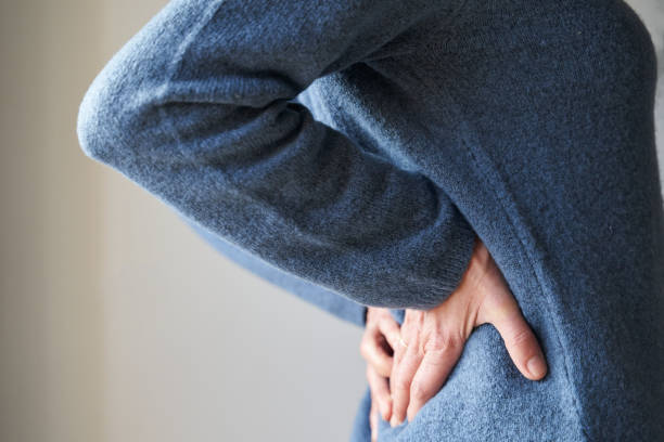 woman with lumbar back pain holds spine with hands in kidney area - low back imagens e fotografias de stock