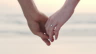 istock An unrecognizable couple holding hands and wearing an engagement ring. Closeup of a man and woman after their proposal at the beach 1396056959