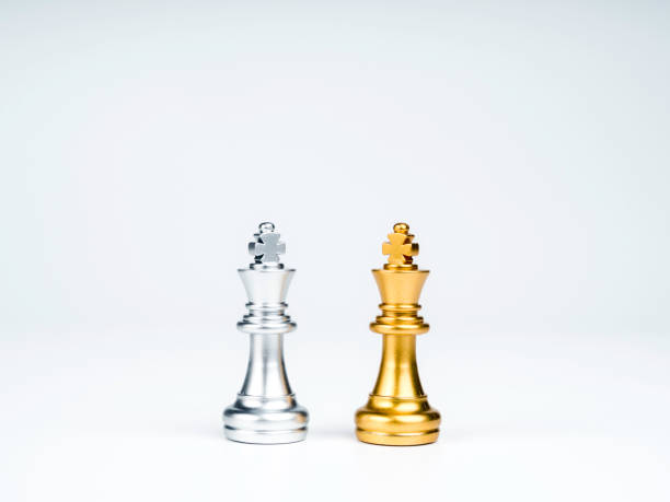 A peça de xadrez do rei dourado em pé no tabuleiro de xadrez na frente de  peças de xadrez de prata em fundo branco com espaço de cópia confronto de  competição de