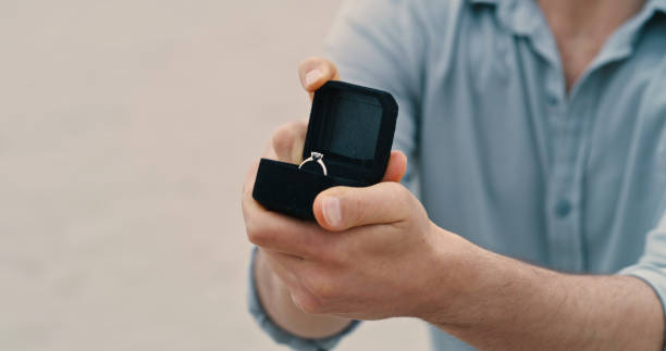 istock An unrecognizable man on bended knee, showing an open box with an engagement ring in it at the beach. Closeup of a man making a wedding proposal 1396057119
