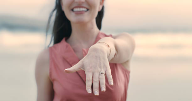 eine unkenntliche und glückliche junge frau, die ihren verlobungsring am strand zeigt. nahaufnahme einer lächelnden frau nach ihrem antrag mit hand und ring - zoom ring stock-fotos und bilder