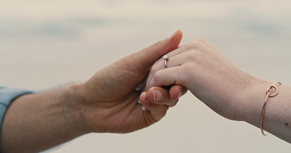 An unrecognizable couple holding hands and wearing an engagement ring. Closeup of a man and woman after their proposal at the beach