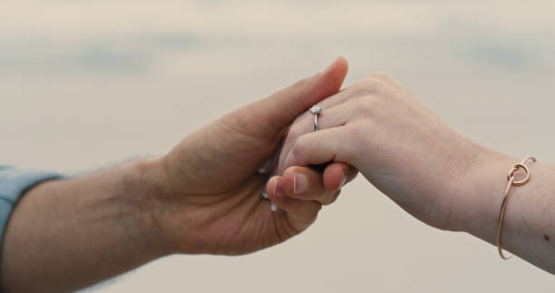 um casal irreconhecível de mãos dadas e usando um anel de noivado. close-up de um homem e uma mulher após sua proposta na praia - eternity wedding beach human hand - fotografias e filmes do acervo
