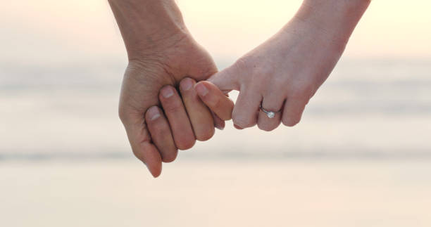 um casal irreconhecível de mãos dadas e usando um anel de noivado. close-up de um homem e uma mulher após sua proposta na praia - eternity wedding beach human hand - fotografias e filmes do acervo
