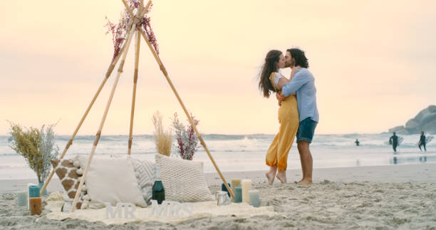 ein glückliches junges paar, das sich nach ihrem antrag am strand umarmt und umarmt. ein verliebter mann und eine verliebte frau, die sich küssen und ihre verlobung feiern - young women wedding married engagement ring stock-fotos und bilder