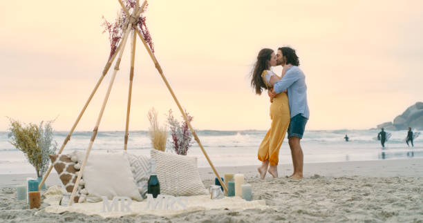 A happy young couple hugging and embracing on the beach after their proposal. A man and woman in love, kissing and celebrating their engagement stock photo