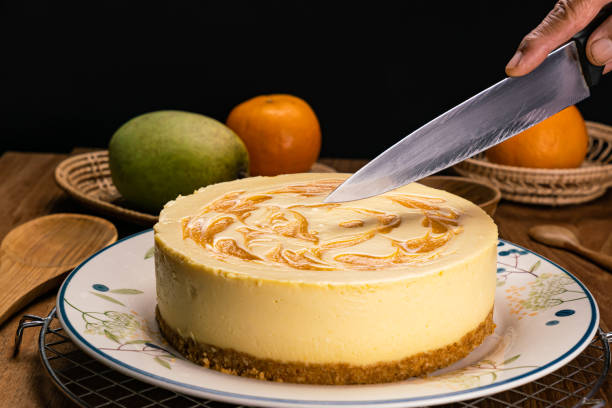uomo che usa il coltello tagliando la cheesecake al mango fatta in casa in piatto di ceramica. - fruit table bamboo black foto e immagini stock