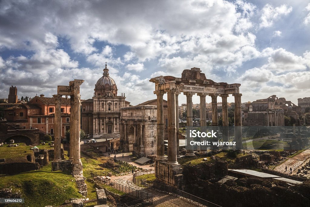 Roman Forum, Italy The Roman Forum in Rome, Italy in the morning. The Temple of Saturn and the Arch of Septimius Severus are visible in the foreground, and the church of Santi Luca e Martina and Temple of Antoninus and Faustina in the background. Ancient Stock Photo