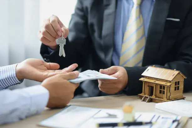 Photo of Real Estate Negotiation. The real estate agent or seller receives money and gives the customer the house keys after the purchase agreement is reached.