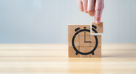 mano de empresario sosteniendo y ensamblando cubo de madera con forma de reloj despertador icono. El concepto de ahorro de tiempo en el trabajo para reducir costes. photo