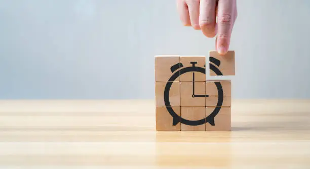 businessman's hand holding and assemble wooden cube with icon alarm clock shape. The concept of saving time on work to reduce costs.