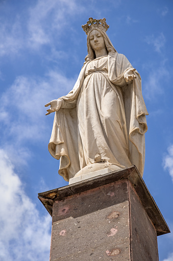 closeup of a stone Jesus statue in a cemetery, with arms outstretched backed by a bright blue sky