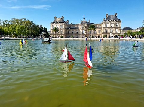 The Jardin du Luxembourg (Luxembourg Garden), is located in the 6th arrondissement of Paris, France. Creation of the garden began in 1612. The image shows model sailboats on the octagonal Grand Bassinin the gardens during a warm day in springtime. In the background visible: The Luxembourg Palace.