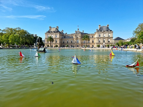 The Jardin du Luxembourg (Luxembourg Garden), is located in the 6th arrondissement of Paris, France. Creation of the garden began in 1612. The image shows model sailboats on the octagonal Grand Bassinin the gardens during a warm day in springtime. In the background visible: The Luxembourg Palace.