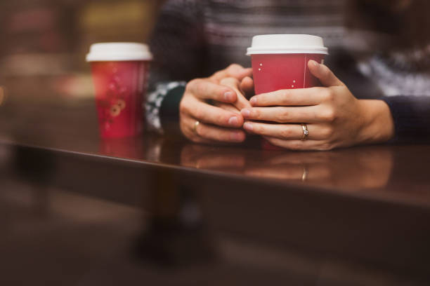 Closeup of a married caucasian couple holding hands and drinking coffee from the disposable paper red cusp. Wedding rings on their hands Christmas romance in the city. cusp stock pictures, royalty-free photos & images