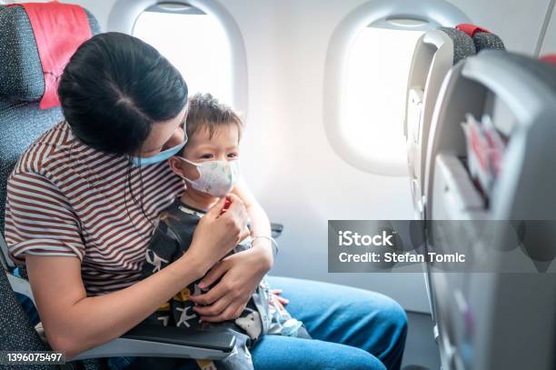 Mother And Her Baby Boy Wearing Surgical Face Mask In An Airplane Baby Traveling In Airplane Flying Sitting On His Mother Lap In The Aircraft Stock Photo - Download Image Now