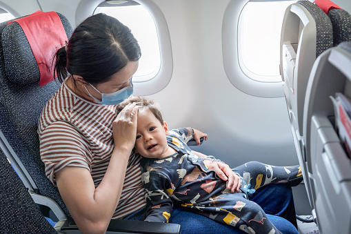 Mother taking airplane with a baby boy. Infant traveling in airplane flying sitting on his mother lap in the aircraft