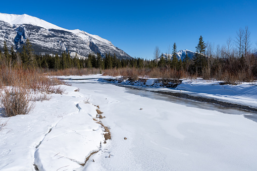 Canadian Rockies beautiful scenery during winter. Snowcapped mountain range, frozen river. Canmore, Alberta, Canada.