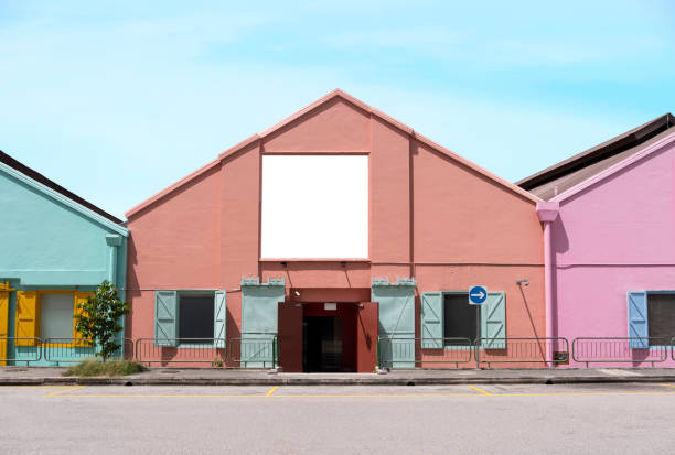 Billboard mock up in suburb background with clear sky. Template of an empty information billboard on colorful buildings near roadside with clear road, Mock-up of banner placeholder and poster.