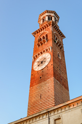 The Torre dei Lamberti in Verona (Italy) in morning sun. Clock tower on blue sky background. Verona is a popular tourist destination of Europe.