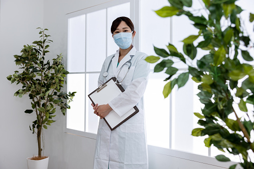 Portrait of female doctor wearing mask and white coat standing in hospital