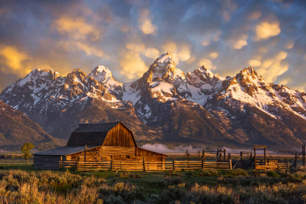 素朴な納屋と雪をかぶった山々の上の日の出の空 - western usa mountain peak landscape farm ストックフォトと画像