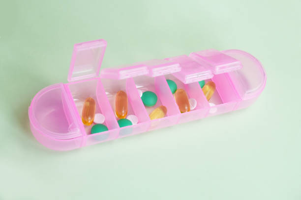 istock Pink plastic organizer for pills and vitamins on a light green background 1396092111