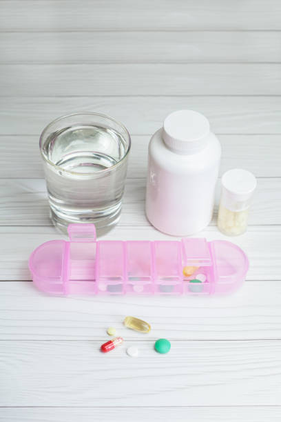 imagem vertical de um organizador de pílulas, um copo de água e frascos de comprimidos - compartimento de arrumação - fotografias e filmes do acervo