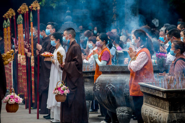 成都、中国 - 2022年5月8日:信者はマスクを着用し、仏陀の誕生日を祝うために温州修道院の集まりで祈ります。 - many colored prayer flags ストックフォトと画像