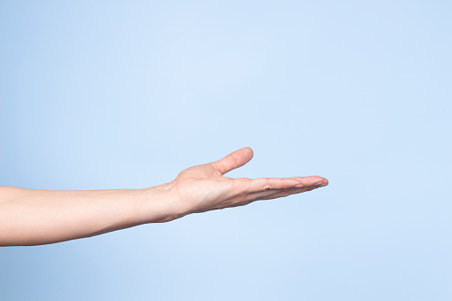 Woman hand gesture. Female open hand on light blue background. Empty palm up pose like holding something. Front view.