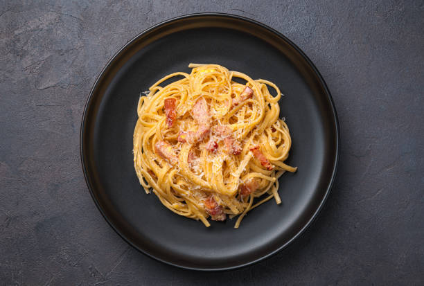 traditionelle italienische pasta carbonara mit speck, parmesan, ei und pfeffer auf dunklem hintergrund. - linguini stock-fotos und bilder