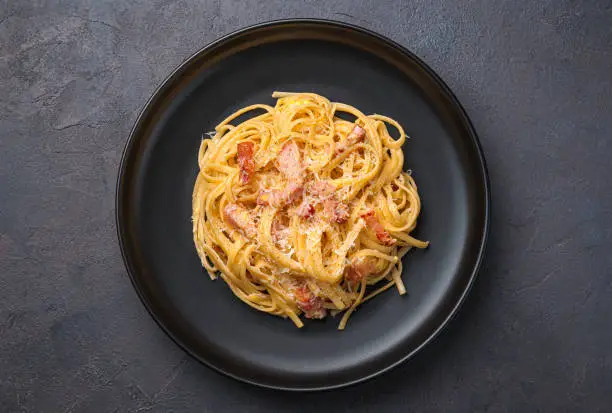 Traditional Italian pasta carbonara with bacon, parmesan, egg and pepper on a dark background. Top view