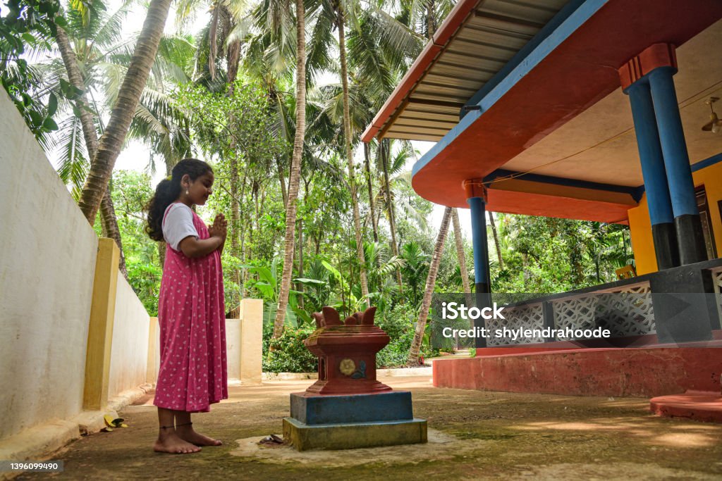 Indian little girl offering prayer to holy basil plant Indian little girl offering prayer to holy basil plant in front of home, kerala Goddess Lakshmi Stock Photo