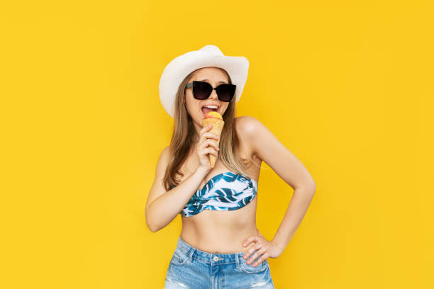 una giovane donna bionda con un cappello bianco e occhiali da sole mangia sorbetto gelato alla frutta in un cono di cialda - cream horn foto e immagini stock