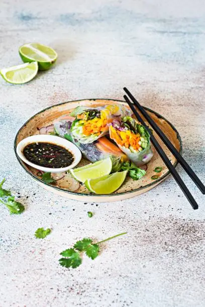 Photo of Fresh Asian appetizer Spring rolls (Nem) made from rice paper and raw vegetables and herbs with hot sauce on a light blue background. Vietnamese Food