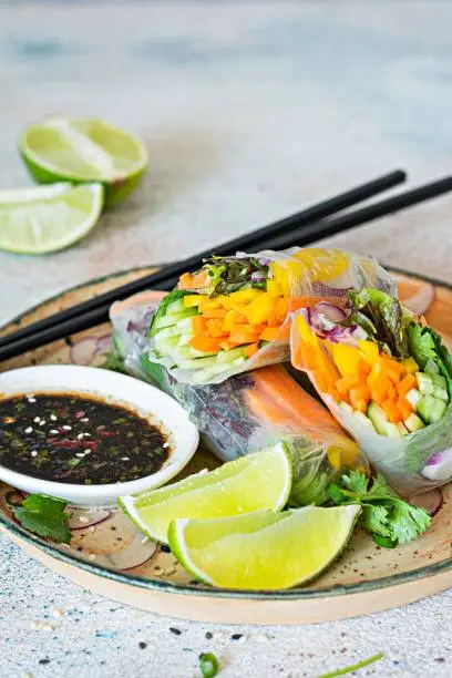 Photo of Fresh Asian appetizer Spring rolls (Nem) made from rice paper and raw vegetables and herbs with hot sauce on a light blue background. Vietnamese Food