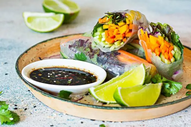 Photo of Fresh Asian appetizer Spring rolls (Nem) made from rice paper and raw vegetables and herbs with hot sauce on a light blue background. Vietnamese Food