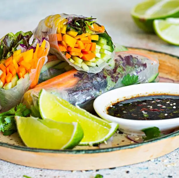 Photo of Fresh Asian appetizer Spring rolls (Nem) made from rice paper and raw vegetables and herbs with hot sauce on a light blue background. Vietnamese Food