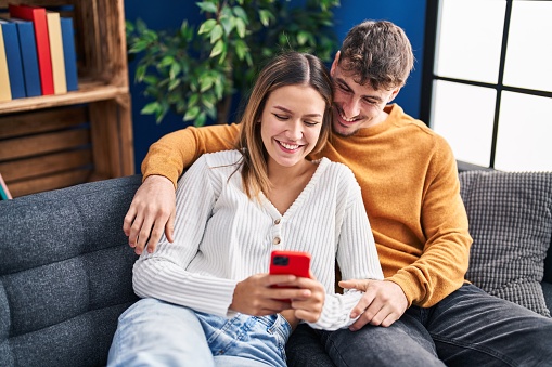 Young man and woman couple using smartphone sitting on sofa at home