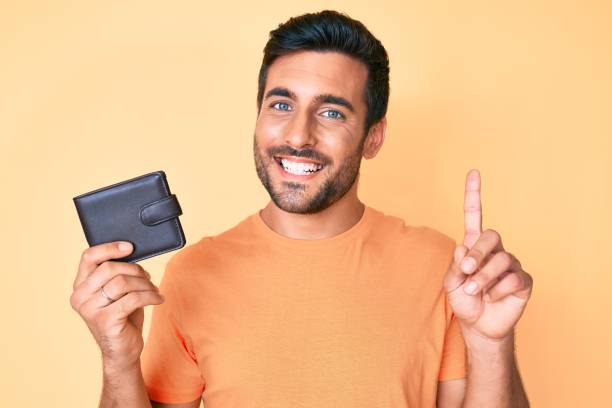 istock Young hispanic man holding leather wallet surprised with an idea or question pointing finger with happy face, number one 1396105333