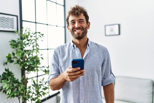 istock Young handsome man using smartphone at home looking positive and happy standing and smiling with a confident smile showing teeth 1396107213
