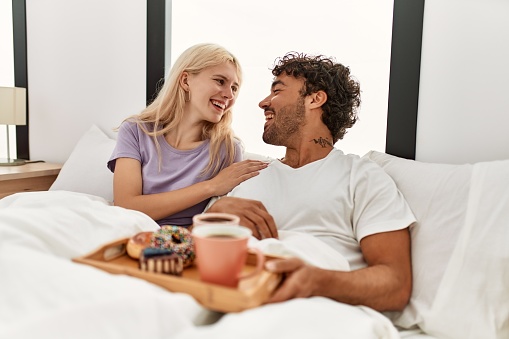 Young beautiful couple smiling happy having breakfast on the bed at home.