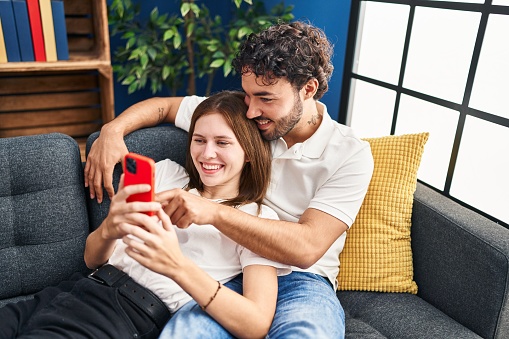 Man and woman smiling confident using smartphone at home