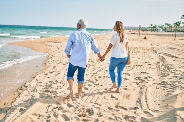istock Middle age hispanic couple walking at the beach on back view. 1396109136