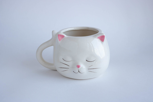 White coffee mug in the shape of a cat with pink ears, close-up on a white background.