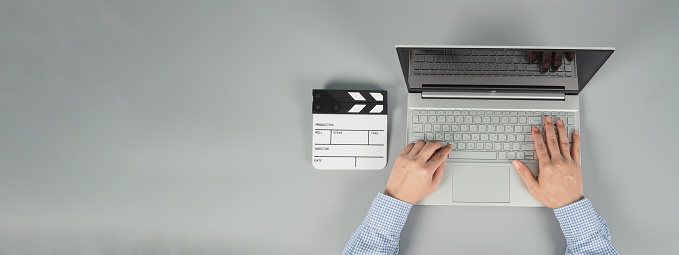 Hands is typing and computer laptop or notebook with black clapperboard or movie slate on grey background.Studio shot.top eye view.